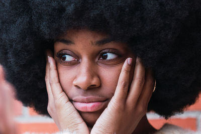 Beautiful african american woman with afro hairstyle and hand on face looking away on brick wall