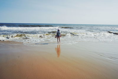 Rear view of woman standing on beach against clear sky