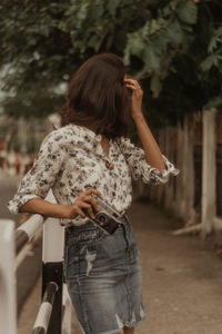 Woman holding camera while standing against railing