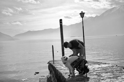 Man wiping dog with towel on pier over lake against mountains