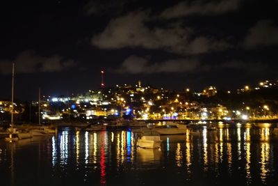 Illuminated buildings by river against sky at night