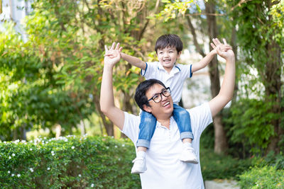 Cheerful father carrying son on shoulder outdoors