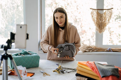 Smiling woman holding garment blogging at home