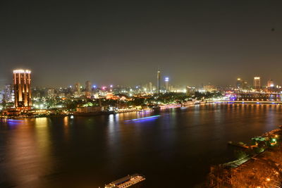 Illuminated city by river against sky at night