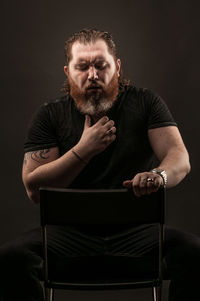 Portrait of man sitting against black background