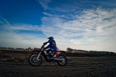 Motocross racer on dirt road against sky
