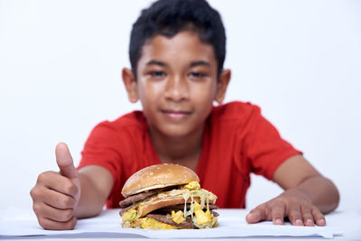 Portrait of boy eating burger against white background