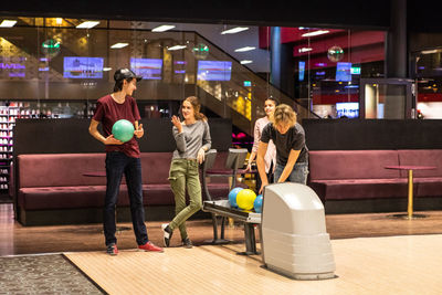 Smiling teenage friends playing on illuminated parquet floor at bowling alley