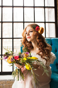 Beautiful young woman with flowers on window