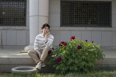 Man looking away while sitting against house