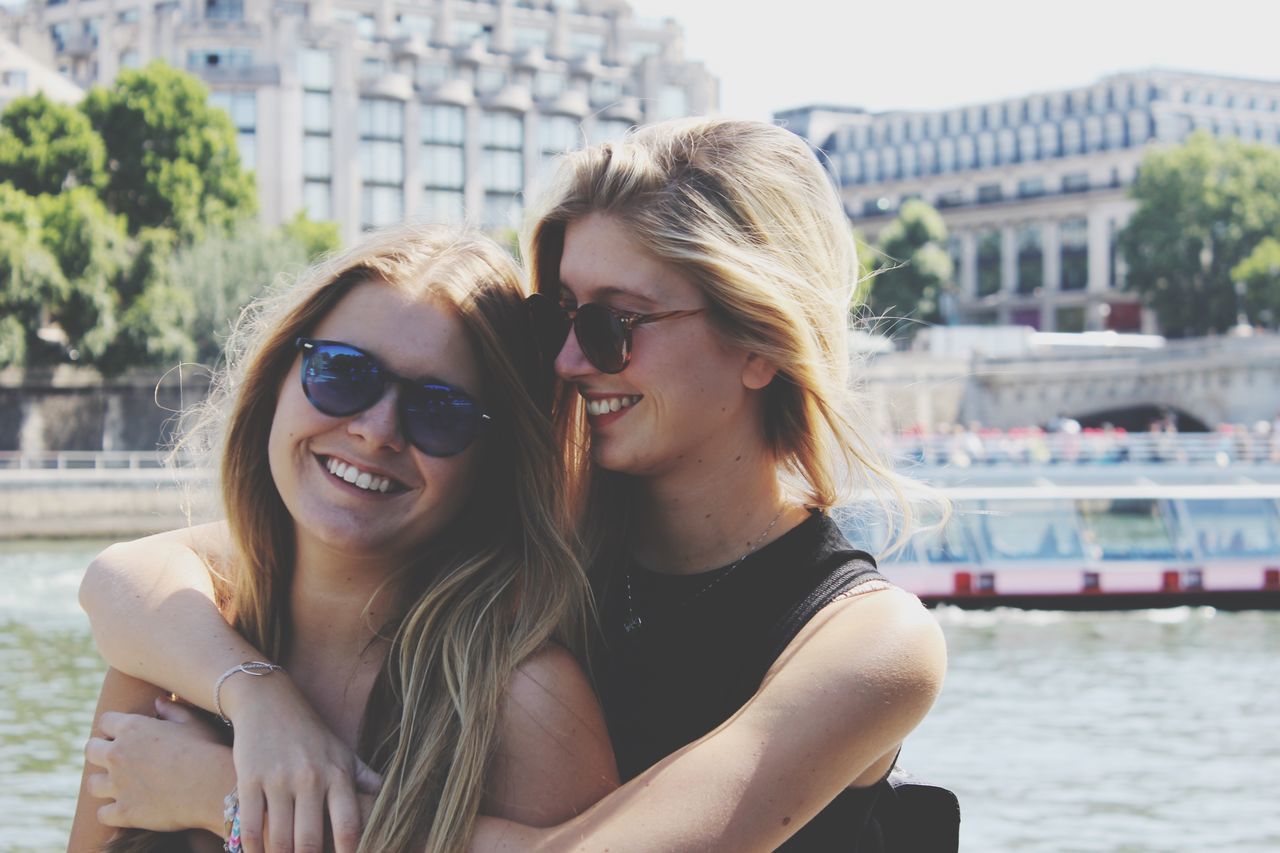 young adult, person, lifestyles, young women, leisure activity, headshot, sunglasses, portrait, looking at camera, smiling, focus on foreground, front view, toothy smile, happiness, building exterior, head and shoulders, long hair