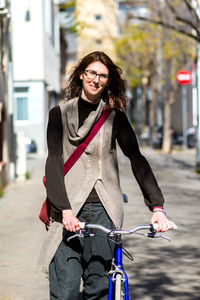 Young smiling woman walking on a city street with bicycle