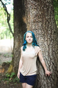 Portrait of a beautiful young woman standing by tree trunk in forest