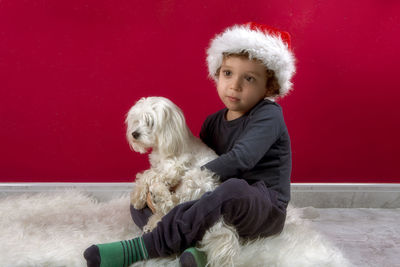 Photo of boy with santa claus hat hugging his puppy