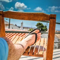 Low section of man relaxing on wood against sky