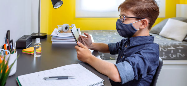 Boy wearing mask studying with digital tablet at home