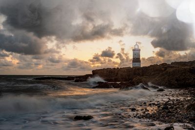 Lighthouse amidst sea and buildings against sky