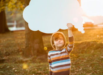 Boy holding speech bubble on field during sunset