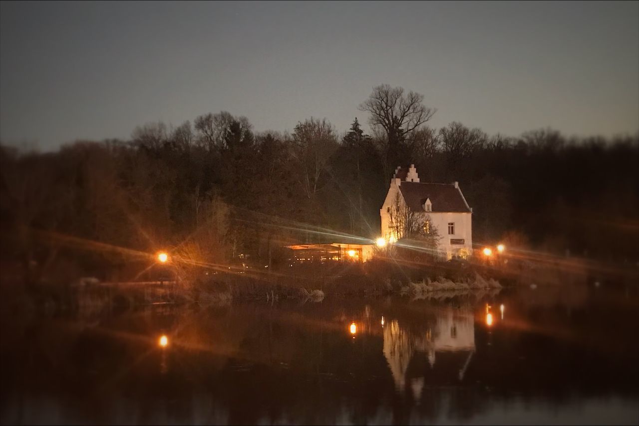 ILLUMINATED BUILDING BY TREES AT NIGHT