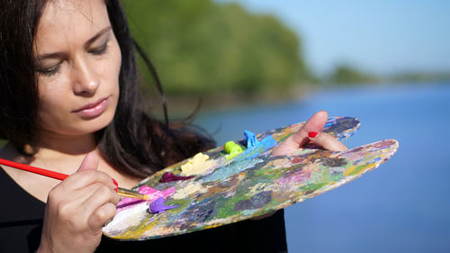 Portrait of a beautiful forty years old brunette woman artist, close-up of a palette with paints