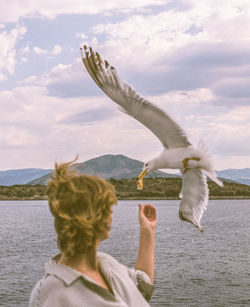 Rear view of woman flying seagull against sky