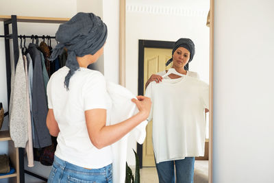 A woman in a white t-shirt tries on clothes in front of a mirror.
