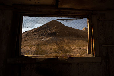 View of hill in desert landscape thru abandoned building window of ghost town 