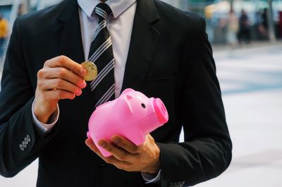 Midsection of businessman inserting coin in pink piggy bank