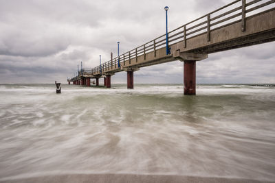 Low angle view of bridge on sea against cloudy sky