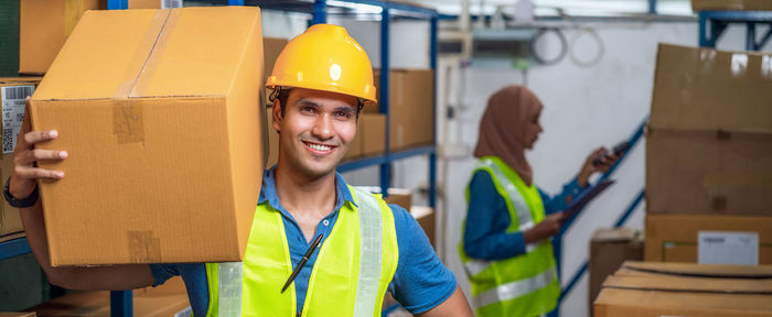 Portrait of smiling worker carrying box in factory