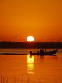 Silhouette people fishing in lagoon against orange sky during sunset