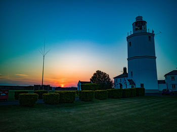 Lighthouse on field against sky during sunset