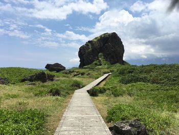 Footpath leading towards rocks against sky