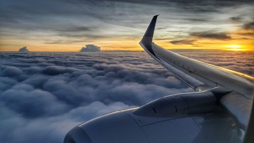 Airplane flying over cloudscape against sky during sunset