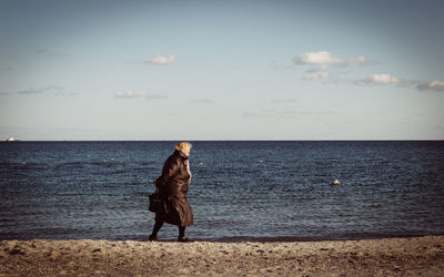 Full length of woman walking on beach against sky