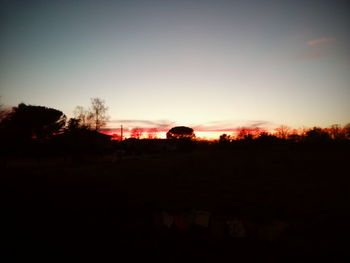 Silhouette trees on field against clear sky during sunset