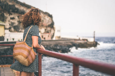 Woman standing by railing at beach against sky