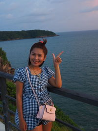 Portrait of smiling young woman standing by sea against sky