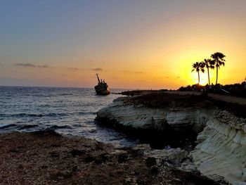 Silhouette rocks on sea against sky during sunset