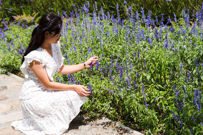Full length of woman crouching by purple flowering plants
