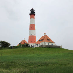 Lighthouse on field by building against sky