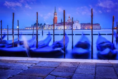 Blurred motion of gondolas moored in sea against city at dusk