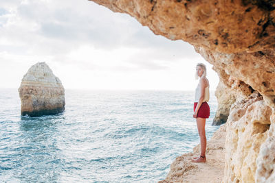 Woman standing on rock by sea against sky