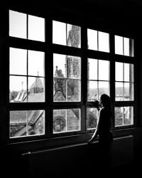 Woman looking through window while standing at home
