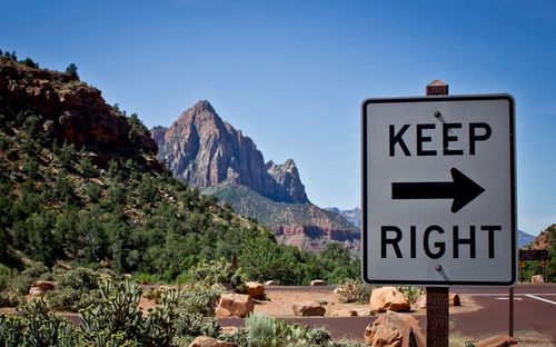 Road sign by mountains against clear sky