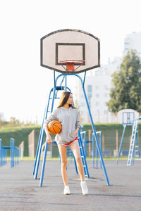 Brunette cheerful young woman dressed in casual modern clothes posing with basketball