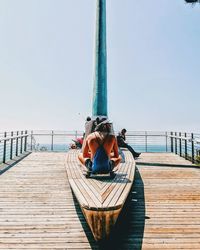 Woman on pier by sea against clear sky