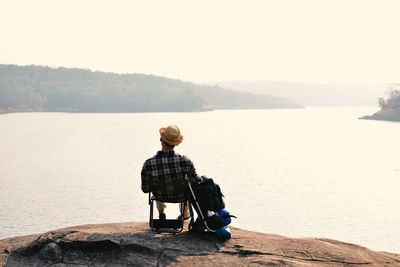 Rear view of man sitting on shore against sky