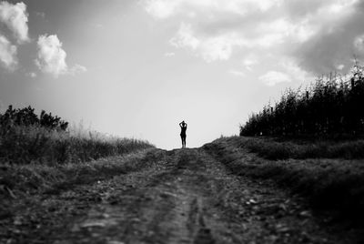 Rear view of woman standing on dirt road against sky
