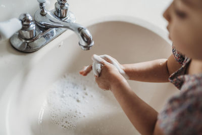 High angle view of young girl washing hands in sink with soap